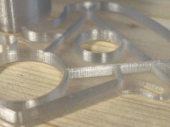 A sustainable 3D-printed cleaning fluid capsule for the Philips smart cleaning system for electric shavers. A transparent print using PCTG on a wooden surface with a blue filament box in the background.