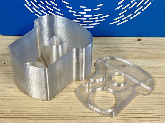 A sustainable 3D-printed cleaning fluid capsule for the Philips smart cleaning system for electric shavers. A transparent print using PCTG on a wooden surface with a blue filament box in the background.
