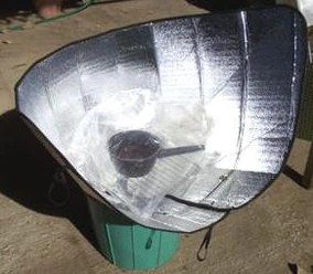 Picture of solar cooker made of folded car sunshade, with a black pot inside a plastic bag in the center