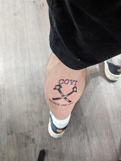 A picture of my left calf from behind showing a pair of ironworking hammers crossed. Above, the letters COYI. Below, the date 2023-06-07
