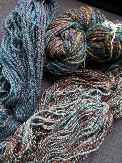 Three skeins of chunky handspun yarn. One blue skein, one light blue and brown/red and one multicoloured skein.