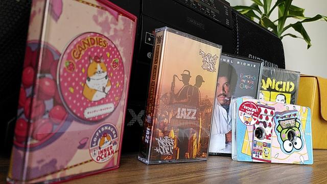 Sharp boombox radio on the back. On the front audio cassettes: Lionel Richie's Dancing in the ceiling;  JazzBastardz by  Raiges Cano / Ness One; Lo-Fi Snacks by various artists;
Tomorrow Never Comes by Rancid. On the right side cassette handbag