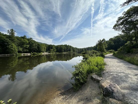 Pandapas Pond in Virginia. A partly cloudy sky is reflected in the pond, with a paved footpath running along side.