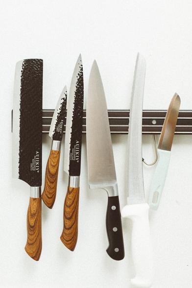 Chefs knives hanging from a magnetic strip attached to a white wall