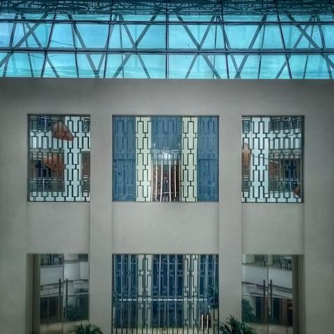 Un pozo de elevador hecho de cristal se refleja en las ventanas del patio interior de un hotel. En el elevador hay alguien.
An elevator shaft is reflected on the windows overlooking a hotel's inner courtyard. There's someone in the elevator.