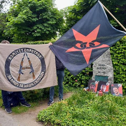 Commemoration event for fallen
 comrades Dmitry Petrov, Finbar Cafferkey and Cooper Andrews in Bern, Switzerland. Their photos are laying on Michael Bakunin's gravestone. Two flags can be seen: of BOAK and Resistance Committee from Ukraine.