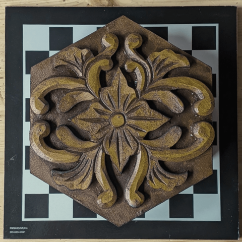 an ornate, hexagonal wooden box carved like a flower on a black and white chess board.