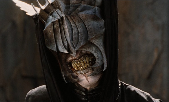 Mouth of Sauron character from Peter Jackson's Return of the King, the finale of his Lord of the Rings trilogy. A sinister figure hooded in black is wearing a helmet that covers its face, and its lips are pulled back to reveal long stained teeth.