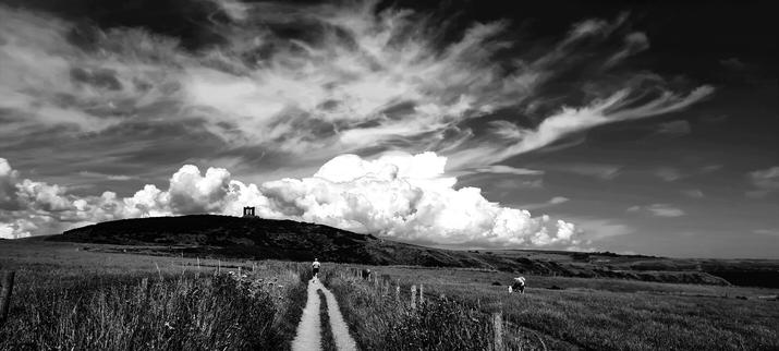 Moody black and white shot of a war memorial on a hill against large white clouds