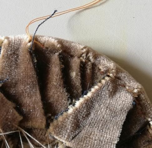 Close up of brown velvet being stitched around a curved edge, using a doubled cotton thread.