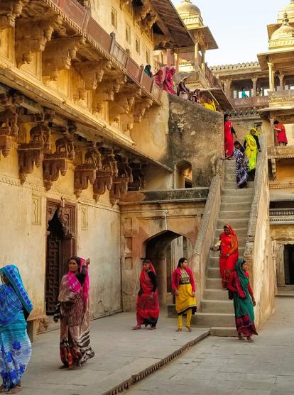 Women in colorful saris descending stone stairs at Jahangir Mahal.