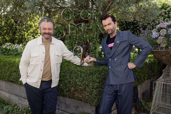 Photo of David Tennant (and Michael Sheen) promoting Good Omens 2. David is in a slim-fitting navy blue double-breasted suit . The t-shirt underneath is black with hot pink writing