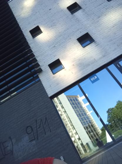 Closeup of a university building, with a small sign saying ULB and the cloudless blue sky and campus reflecting in the window