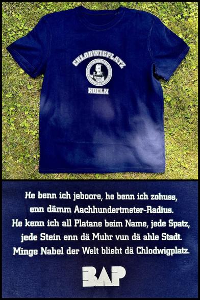 Oben: Das altbekannte blaue Chlodwigplatz-Shirt mit dem kreisförmigen Schriftzug „Chlodwigplatz Köln“ und dem dazwischen aufgedruckten Severinstorbogen.
Unten der Textauszug: „He benn ich jeboore, he benn ich zohuss, enn däm Aachhundertmeter-Radius.
He kenn ich all Platane beim Name, jede Spatz, jede Stein enn dä Muhr vun dä ahle Stadt.
Minge Nabel der Welt blieht dä Chlodwigplatz.“