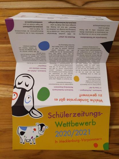 Foto eines Flyers der auf einem Holztisch liegt: "Schülerzeitungs-Wettbewerb 2021/2022 in Mecklenburg-Vorpommern"