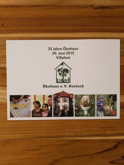 Foto einer Postkarte die auf einem Holztisch liegt: "25 Jahre Ökohaus 20. Juni 2015 Villafest - Ökohaus Rostock"