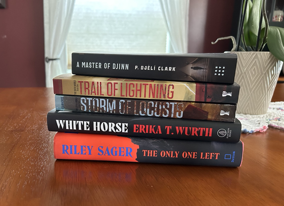 Five stacked books of fiction on top of a wooden table with an orchid behind it.