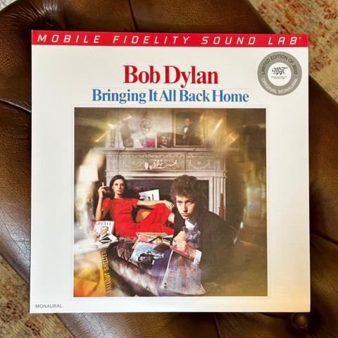 Photo of a record album cover. 

The jacket is a photo of a young Bob Dylan and woman (his manager’s wife, if I recall correctly) in a vivid red dress. Dylan and the woman are sat in front of a fireplace surrounded by miscellany - magazines, a fallout shelter sign. Dylan is cradling a cat. 

Above the picture red and blue text reads, ‘Bob Dylan, Bringing It All Back Home’.