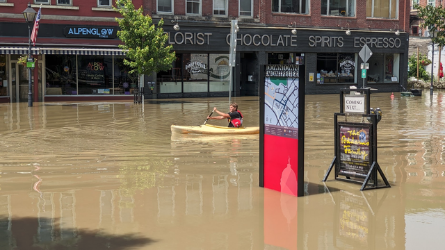 A young man kayaks through brown water down Main Street past a sign with a map of Montpelier.