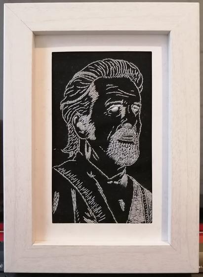 Handembroidery of Izzy Hands' face from Our Flag Means Death. The fabric is black, the threads are grey and silver. It has a white frame.