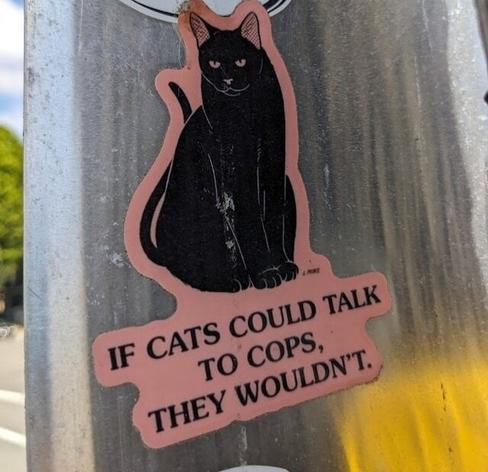 Sticker on a pole featuring a cat and the words "If cats could talk to cops, they wouldn't"