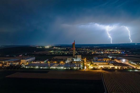 Luftaufnahme bei Nacht und Gewitter von einem Industriegebiet bei Ulm-Jungingen. Dahinter sieht man die Lichter des Stadtteils Lehr. Am wolkenverhangenen Himmel sind rechts zwei Blitze zu sehen.