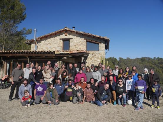 Un grup de persones posant per a la càmera. Darrrere, una casa de muntanya