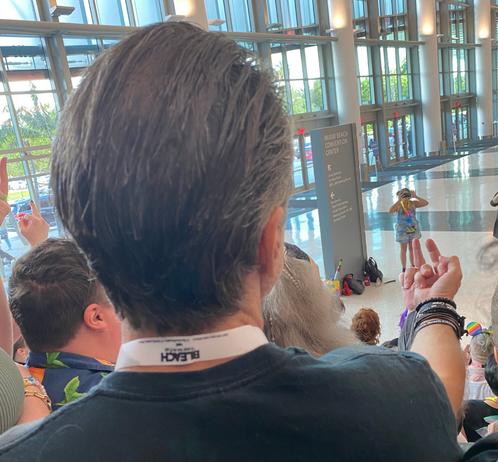 A close-up shot of the back of Con O'Neill's head and his right hand lifted to flip off the camera at the bottom of a stairway (in the middle of a group shot)