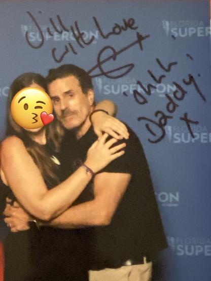 Me in a black dress (with a kissy-face emoji over my face) facing/hugging Con O'Neill in a black t-shirt in front of a blue background. Signature from Con saying "Jill, with love (his signature) Ohhh Daddy! x" on it