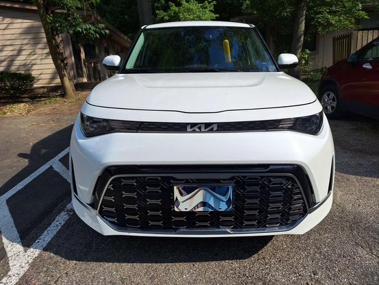 Front view of a blindingly white 2023 Kia Soul with black trim and a vanity plate with a closeup image of an Imperial Stormtrooper. The plate is almost redundant as it appears to capture the angles and overall demeanor of the car it's attached to
