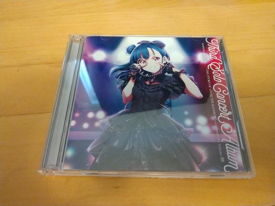 A picture of the CD case for Yoshiko Tsushima's 3rd solo album. The cover features Yoshiko in a black dress, holding a monocle to her right eye and making a "V" with her left hand. The text on the right side of the cover reads:
"Third Solo Concert Album
LoveLive! Sunshine!! ~THE STORY OF "OVER THE RAINBOW"~ starring Tsushima Yoshiko"