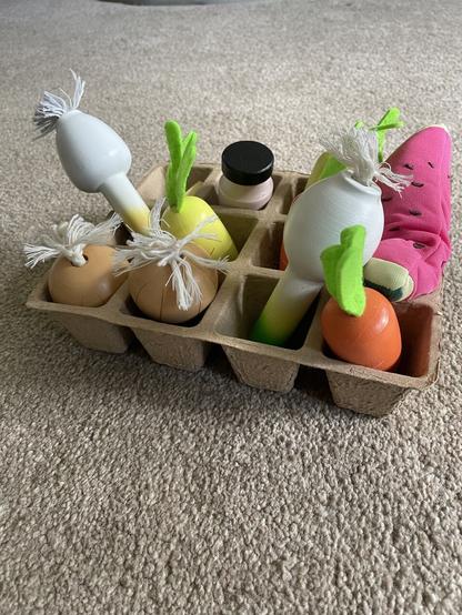 A photo of a seed tray with wooden veggies on each space.