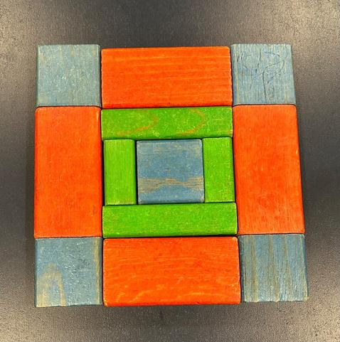 Arrangement of blocks in a square. 5 square blue blocks , 4 red rectangular blocks, 4 green skinny rectangular blocks (2 long and 2 short) arranged symmetrically.