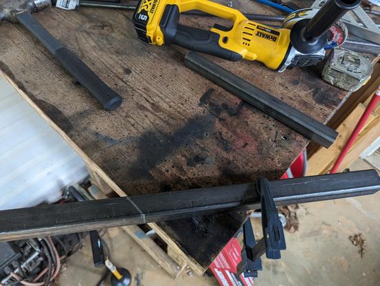 A steel bar clamped to a wooden bench ready to be butchered by the angle grinder sitting next to it