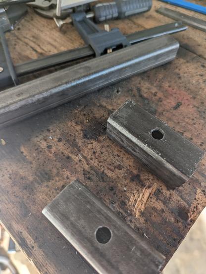 2 3-inch pieces of square tube steel with bolt holes drilled in them. They'll be used to secure other, smaller steel inside the tube when assembled.