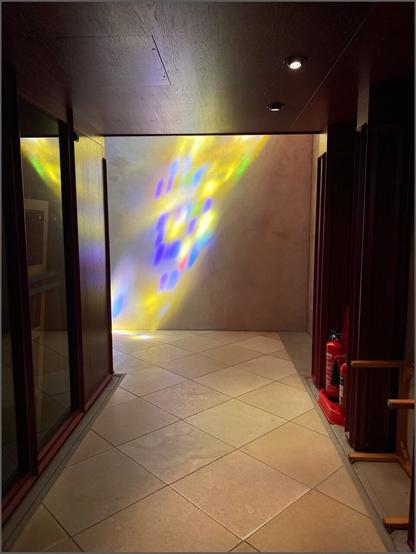 in einer Kirche ein Weg unter der rötlichbraunen Orgel hindurch mit Ausblick auf eine farbig beleuchtete Wand