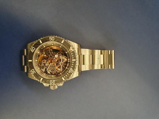 Goldene Luxusuhr mit Ziffernblatt und Blick auf die Zahnräder des Uhrenmechanismus.