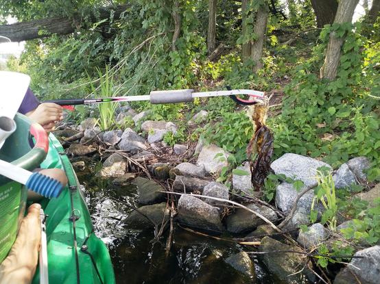 Ein Kind hebt mit der Müllzange eine Plastiktüte aus der Spree in die Mülltonne