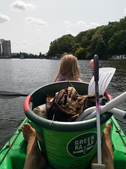 Grünes Kayak von Green Kayak im Wasser. Eine gut gefüllte Mülltonne steht in der Mitte vom Boot.