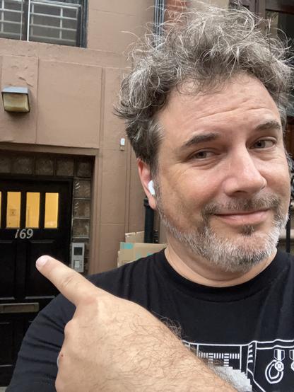 Podsothoth host @todb@infosec.exchange in front of 169 Clinton Street, Lovecraft’s apartment building. He is pointing at the street number, “169.” Nice.