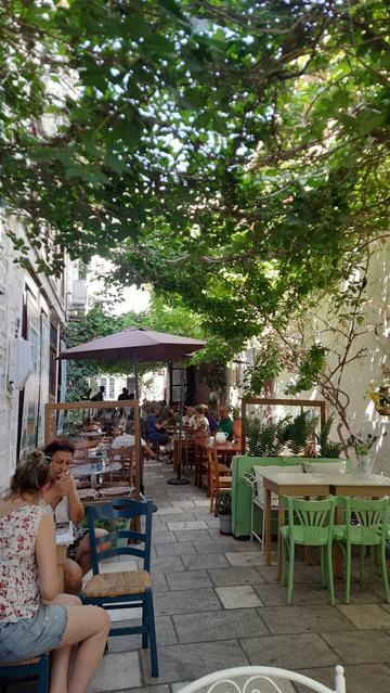 A cosy ally, Peloponnysou street, in Ermoupoli, with people having breakfast under the shade of leaves