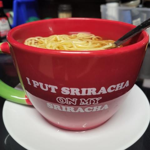 A red mug (cup? bowl?) that says 'I put sriracha on my sriracha' that I found at Goodwill. It has ramen in it, and a fork handle sticking out. It's on my kitchen counter cooling. I have a ramen addiction. Please send help. Lol