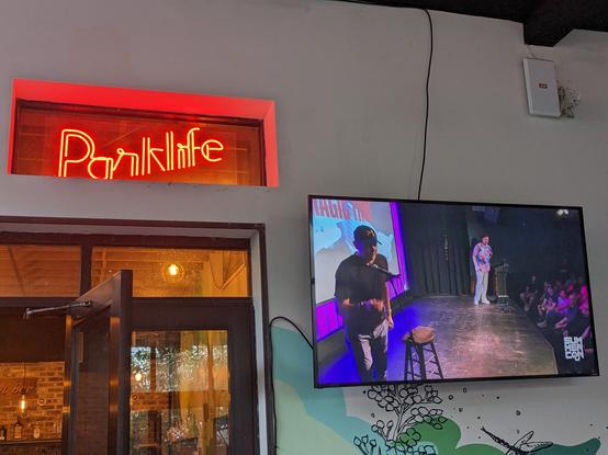 The Parklife logo in Brooklyn right next to a TV presenting a live broadcast of SummerCon going on at Littlefield.