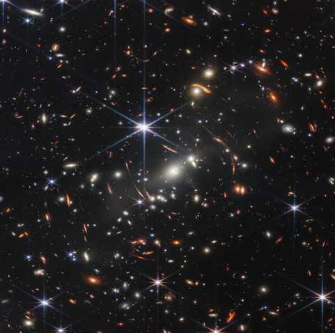 Deep field image showing ancient galaxies and other large structures, some distorted by gravitational lensing.