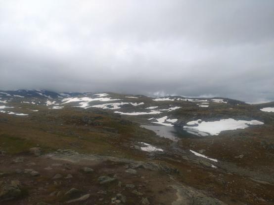 Lave og runde fjell med snøflekker og vann og et lavt grått skydekke