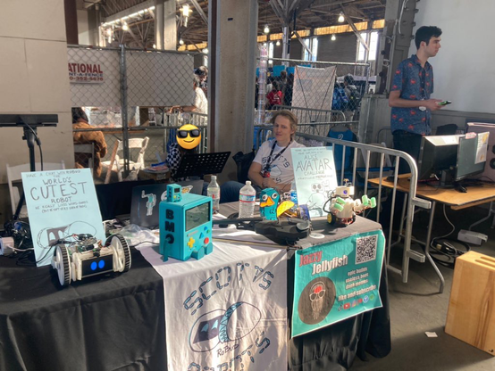 Tired crew behind the ScottsRobots booth D3.10 at golden hour.