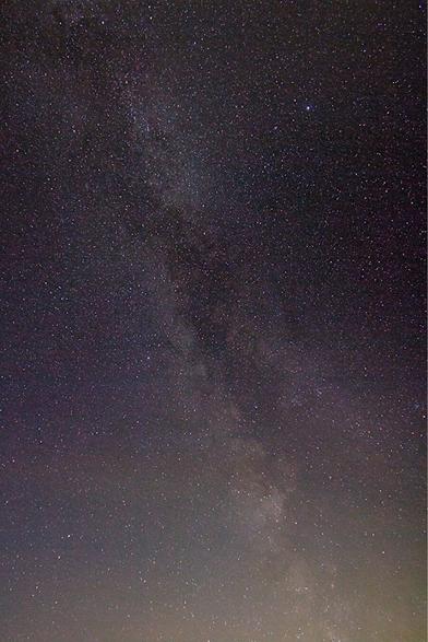 Photograph of a really starry night sky with with the milky way. The sky is slightly purple with a gradient to yellow/orange in the bottom because of the light pollution.