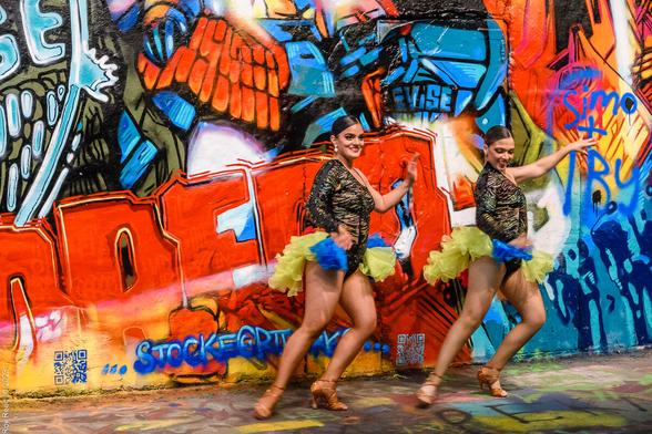 Two women dancing in front of a vibrant street art mural.