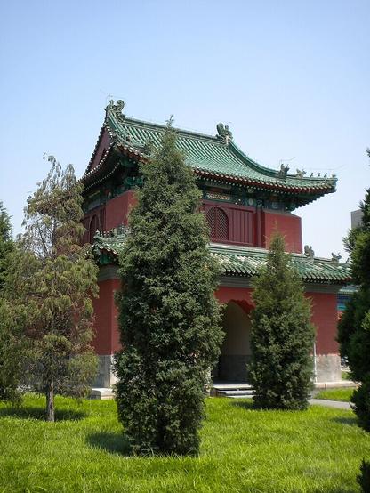 1st or 2 WikiCommons color photos of a deep terracotta red building with curving decorative green roofing and a large arched entryway that goes all the way through, and other architectural features. This temple is partially obscured by trees planted around it.

Caption: "月坛钟楼/Bell Tower (Temple of the Moon)"
Photo by Dirrival, 2009.

https://commons.wikimedia.org/wiki/File:Bell_Tower2(Temple_of_Moon).JPG