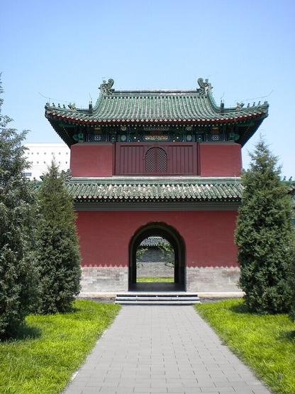 2nd or 2 WikiCommons color photos of a deep terracotta red building with curving decorative green roofing and a large arched entryway that goes all the way through, and other architectural features. This temple is partially obscured by trees planted around it.

Caption: "北京月坛钟楼/Bell Tower (Temple of the Moon)"
Photo by Dirrival, 2009.

https://commons.wikimedia.org/wiki/File:Bell_Tower(Temple_of_Moon).JPG